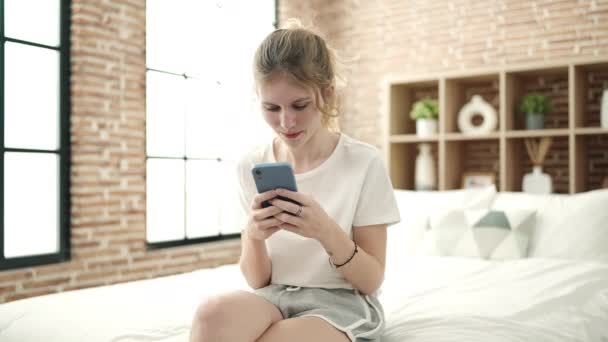 Νεαρή Ξανθιά Γυναίκα Που Χρησιμοποιεί Smartphone Κάθεται Στο Κρεβάτι Στο — Αρχείο Βίντεο