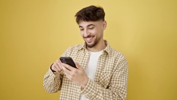 若いアラブ人男笑顔自信を持って使用してスマートフォン隔離された黄色の背景 — ストック動画
