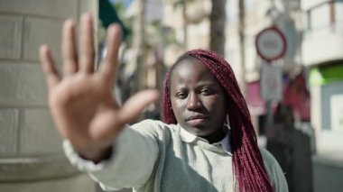 Saçları örgülü Afrikalı bir kadın sokakta el hareketlerini durduruyor.