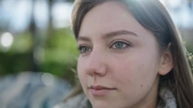 Genç sarışın kadın parkta rahat bir ifadeyle yan tarafa bakıyor.