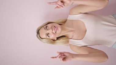 Genç sarışın kadın gülümsüyor. Kendine güvenen, pembe arka planda parmaklarıyla işaret eden.