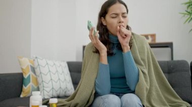 Genç, güzel, İspanyol bir kadın telefonda konuşuyor. Kanepede oturuyor ve evde hasta yatıyor.
