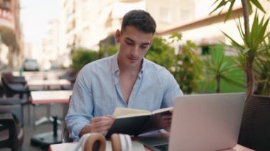 Latin asıllı genç adam kahve dükkanının terasında ders çalışıyor.