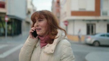 Middle age redhead woman smiling confident talking on the smartphone at street