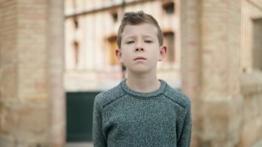 Rahat yüzü olan sarışın çocuk sokakta jest yapıyor.