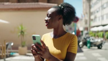 Afro-Amerikalı kadın sokakta akıllı telefon kullanarak kendine güveniyor.