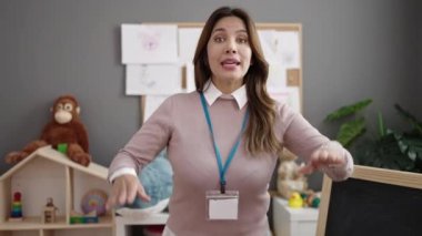 Young beautiful hispanic woman preschool teacher asking for silence at kindergarten