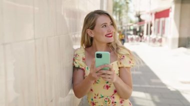Genç, güzel, İspanyol bir kadın sokakta akıllı telefon kullanarak gülümsüyor.