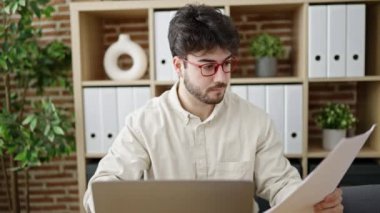 Genç İspanyol iş adamı ofiste dizüstü bilgisayar okuma belgesi kullanıyor.