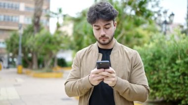 Genç İspanyol adam parkta gülümseyen akıllı telefon kullanıyor.