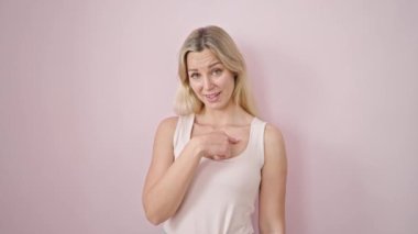 Genç sarışın kadın kendini gösterip, pembe arka planda parmağıyla 