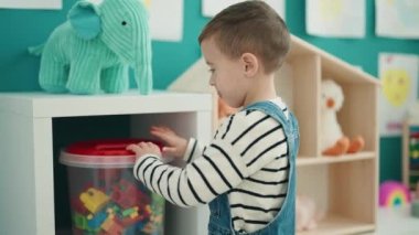 Adorable caucasian boy holing cube with construction blocks at kindergarten