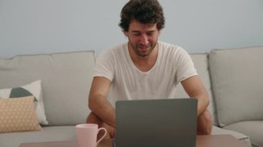 Genç İspanyol adam dizüstü bilgisayar kullanıyor ve evde kahve içiyor.