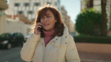 Middle age redhead woman smiling confident talking on the smartphone at street