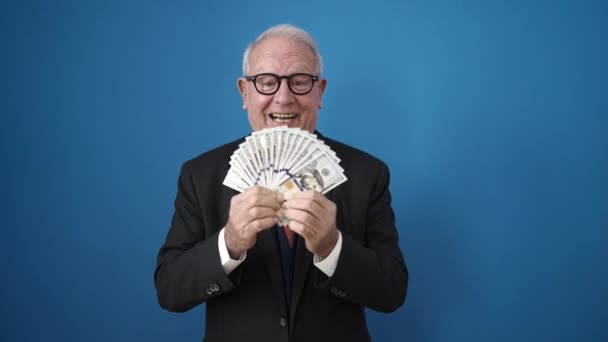Senior Lächelt Zuversichtlich Und Wirft Dollars Über Isolierten Blauen Hintergrund — Stockvideo