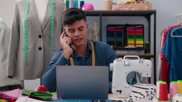 Młody Latynos Krawiec Rozmawiający Smartfonie Przy Użyciu Laptopa Fabryce Ubrań — Wideo stockowe