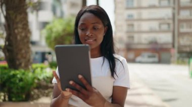 Genç Afrikalı Amerikalı kadın parkta dokunmatik ped kullanarak gülümsüyor.