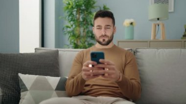 Evdeki kanepede oturan, akıllı telefon kullanan genç bir İspanyol.