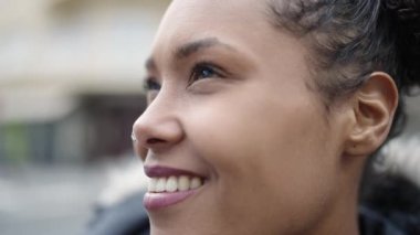 Afro-Amerikalı kadın gülümsüyor. Kendinden emin bir şekilde caddeye bakıyor.