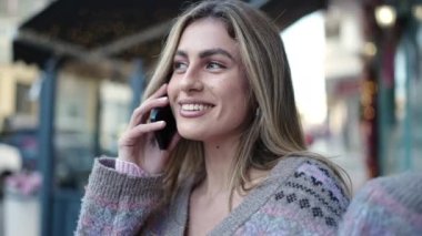 Genç sarışın kadın gülümsüyor. Kendine güveni tam. Akıllı telefondan konuşuyor.