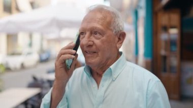 Senior grey-haired man smiling confident talking on the smartphone at street