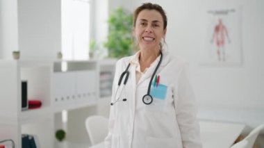 Klinikte dikilen orta yaşlı kadın doktor üniforması giyiyor.