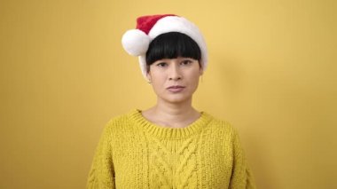 Sarı arka planda kendine güvenen genç Çinli kadın Noel şapkası takıyor.