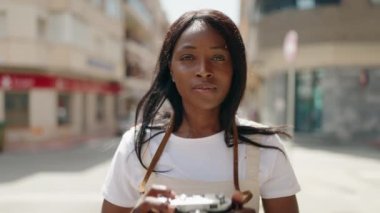Genç Afrikalı Amerikalı kadın caddede klasik kamera kullanıyor.
