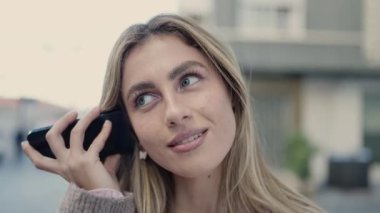 Young blonde woman smiling confident listening audio message by the smartphone at street