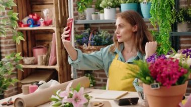 Young beautiful hispanic woman florist make selfie by smartphone sitting on table at florist