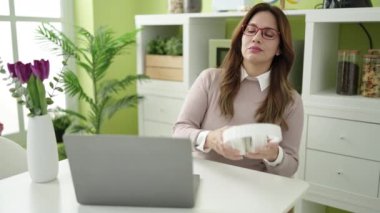 Young beautiful hispanic woman using laptop and headphones sitting on table at home