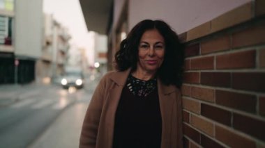 Orta yaşlı İspanyol kadın sokakta kendine güvenerek gülümsüyor.