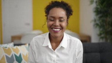 Afro-Amerikalı bir kadın evdeki koltukta video görüşmesi yapıyor.
