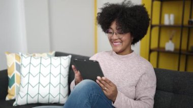 Young african american woman using touchpad sitting on sofa at home