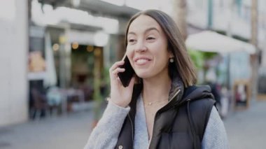 Genç, güzel, İspanyol bir kadın gülümsüyor. Akıllı telefondan konuşuyor.