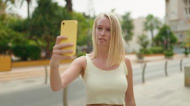 Young blonde woman smiling confident having video call at park