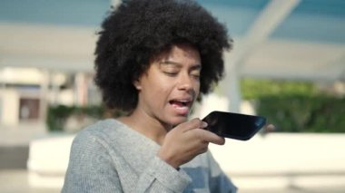 Afro-Amerikalı kadın gülümsüyor. Parktaki akıllı telefondan konuşuyor.