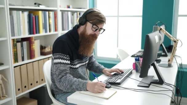 Young Redhead Man Student Using Computer Headphones Writing Notebook Library — Αρχείο Βίντεο