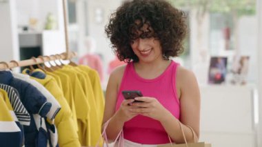 Ortadoğulu genç bir bayan müşterimiz elbise mağazasında akıllı telefon kullanarak gülümsüyor.