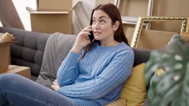 Yeni evindeki kanepede oturan beyaz bir kadın akıllı telefondan konuşuyor.