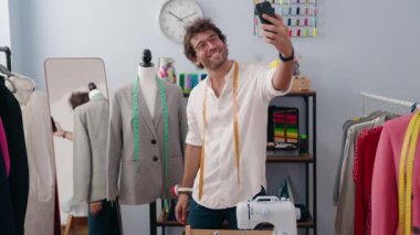 Young hispanic man tailor smiling confident make selfie by smartphone at clothing factory