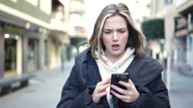 Sokakta akıllı telefon kullanan genç sarışın kadın.