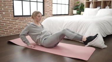 Young blonde woman stretching and working out at bedroom