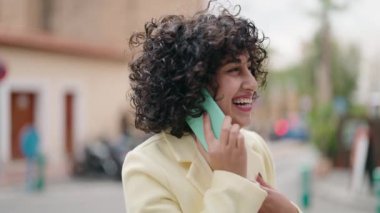 Gülümseyen genç bir kadın caddedeki akıllı telefondan konuşuyor.