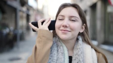 Young blonde woman smiling confident listening audio message by the smartphone at street