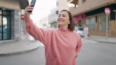 Orta yaşlı kadın gülümsüyor. Sokakta akıllı telefonun yanında özçekim yapıyor.