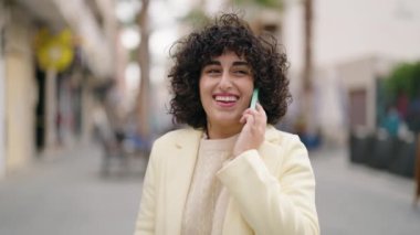 Gülümseyen genç bir kadın caddedeki akıllı telefondan konuşuyor.