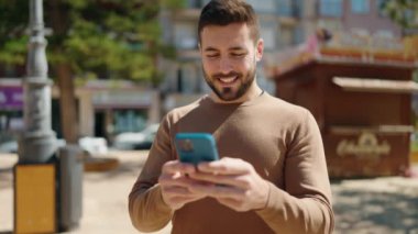 Parkta akıllı telefon kullanarak gülümseyen İspanyol genç adam.
