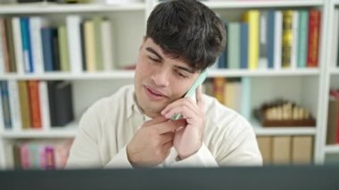 Genç İspanyol öğrenci bilgisayar kullanıyor. Akıllı telefondan konuşuyor. Kütüphanede okuyor.