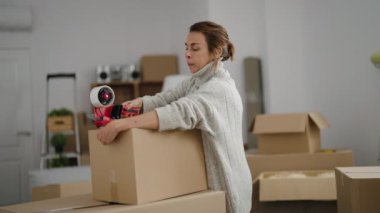 Orta yaşlı bir kadın yeni evinde karton kutu paketliyor.